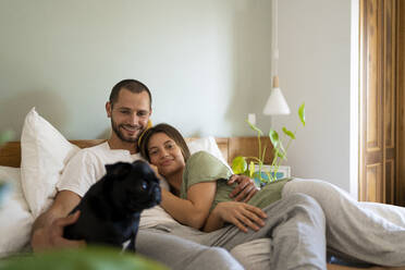 Glückliches Paar mit Mops auf dem Bett liegend zu Hause - SBOF03195