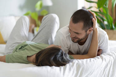 Glückliches junges Paar kuschelnd auf dem Bett zu Hause - SBOF03207