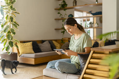 Young woman using digital tablet while sitting on sofa at home - SBOF03229