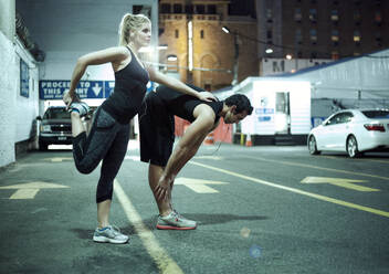 Couple doing stretching exercise during night on road in city - AJOF01279