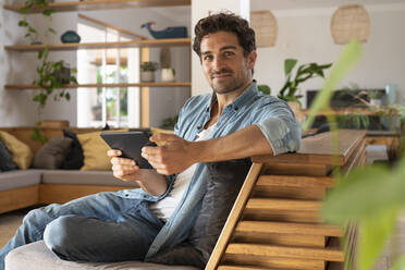 Handsome man with digital tablet sitting on couch in living room - SBOF03235