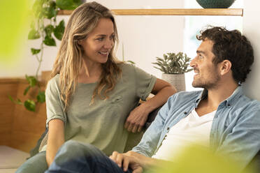 Lächelnde Freundin schaut ihren Freund an, während sie auf dem Sofa im Wohnzimmer sitzt - SBOF03251