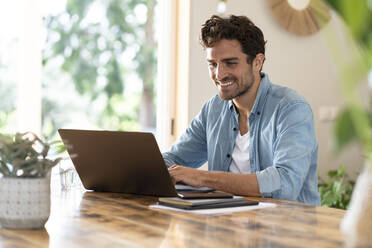 Smiling freelance worker using laptop while sitting at table - SBOF03254