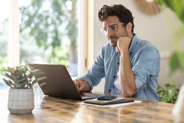Serious male freelancer with head in hands working on laptop at home office - SBOF03261