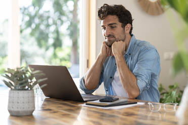 Thoughtful male freelancer with head in hands looking at laptop - SBOF03262