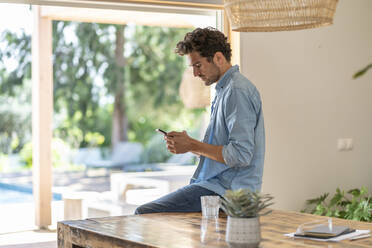 Concentrated man using smart phone while leaning on table - SBOF03271