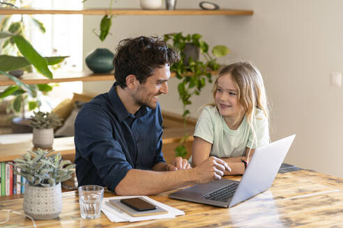 Lächelnder Vater und lächelnde Tochter schauen sich zu Hause vor dem Laptop an - SBOF03292