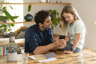 Man showing smart phone to daughter while discussing at home - SBOF03294