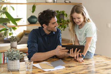 Glücklicher Vater mit digitalem Tablet, der seine Tochter beim Diskutieren zu Hause ansieht - SBOF03295