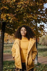 Beautiful Afro woman with hands in pockets standing in park during sunny day - TCEF01683