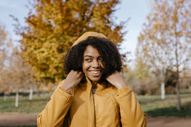 Lächelnde junge Frau, die wegschaut, während sie an einem sonnigen Tag im Park steht - TCEF01685