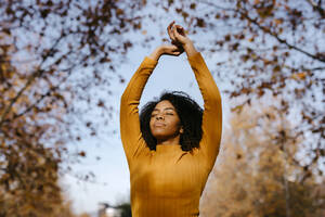 Afro-Frau mit erhobenen Händen im Park an einem sonnigen Tag - TCEF01688