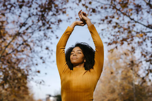 Afro woman with hands raised in park during sunny day - TCEF01688