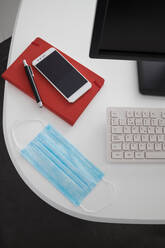 Von oben modernen Computer und Smartphone mit Notebook auf weißen Tisch mit medizinischen Maske in hellen Büro platziert - ADSF21978