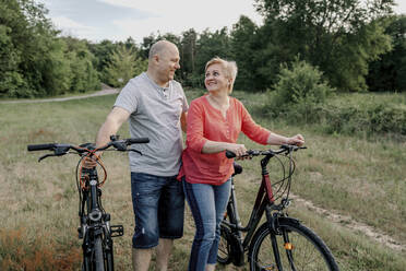 Lächelndes reifes Paar mit Fahrrad auf einem Feld - OGF00958