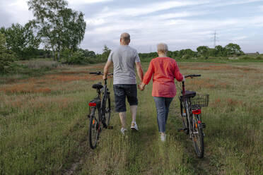 Älteres Paar hält sich an den Händen, während es mit dem Fahrrad auf einem Feld fährt - OGF00959