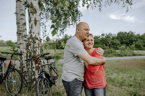 Reifer Mann umarmt Frau, während er auf dem Feld steht - OGF00960