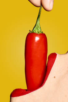 Crop anonyme Frau Mund mit rotem Lippenstift Essen reifen Chili-Pfeffer mit scharfen Geschmack gegen gelben Hintergrund - ADSF22012