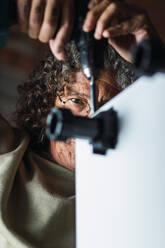 Concentrated unrecognizable senior male furniture maker with curly hair using screwdriver while fixing plinth legs to cabinet in workshop - ADSF22027