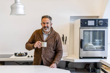 Lächelnder Mann mit Kaffeetasse in der Küche zu Hause stehend - DLTSF01662