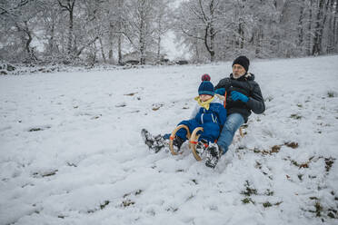 Playful father and son sledding down snowy hill during winter - MFF07636