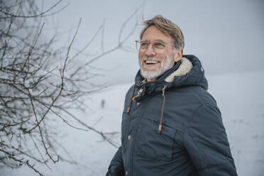 Cheerful mature man standing at snowy field during winter - MFF07638