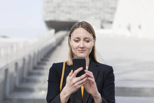 Geschäftsfrau beim Entsperren des Mobiltelefons mit Gesichtserkennungstechnologie im Freien - EIF00634