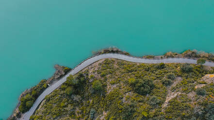 Luftaufnahme einer Landstraße, die sich am Ufer eines türkisfarbenen Sees entlangzieht - OCAF00649