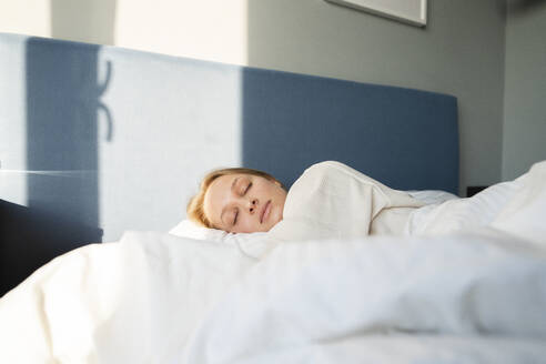 Young woman with blanket lying on bed at home - VPIF03731