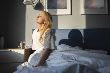 Sunlight on woman sitting with eyes closed on bed at home - VPIF03747