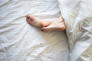 Woman legs crossed at ankle on bed - VPIF03753