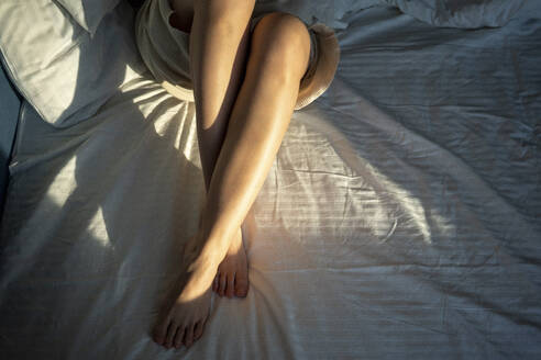 Sonnenlicht auf dem Bein einer Frau auf dem Bett zu Hause - VPIF03754