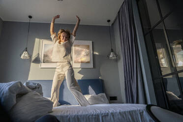 Glückliche Frau tanzt auf dem Bett stehend am Morgen - VPIF03766