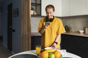 Woman taking photo of breakfast through mobile phone while standing in kitchen - VPIF03776