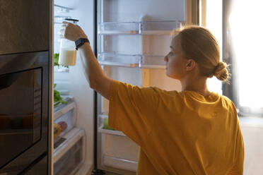 Woman putting milk bottle in fridge at home - VPIF03781