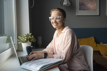 Lächelnde Frau mit Brille sitzt zu Hause am Laptop - VPIF03791
