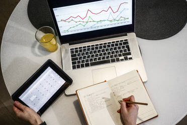 Woman with laptop and digital tablet writing in book on table - VPIF03795