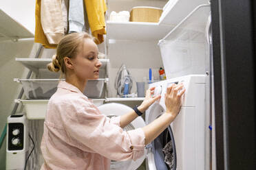 Woman using washing machine in utility room at home - VPIF03814