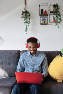 Smiling businessman with headphones using laptop while sitting at home - AGOF00092