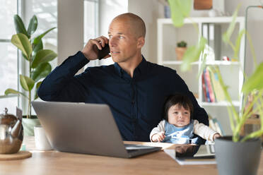 Vater spricht mit seinem Smartphone, während er sein kleines Mädchen zu Hause hält - SBOF03297