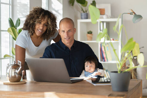 Mutter, Vater und Tochter schauen zu Hause auf den Laptop - SBOF03298