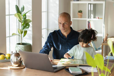 Männlicher Unternehmer, der mit seiner Tochter an einem Laptop arbeitet, während er zu Hause arbeitet - SBOF03304
