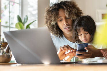 Mother multi-tasking while working on smart phone with daughter in home office - SBOF03317