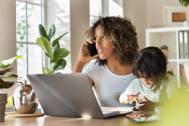 Mutter telefoniert mit ihrem Smartphone, während ihre Tochter zu Hause am Laptop spielt - SBOF03318