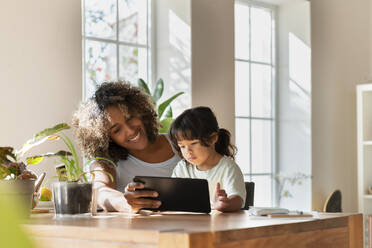 Smiling mother and daughter looking at digital tablet while sitting in living room - SBOF03319