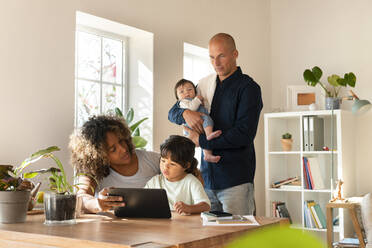 Familie mit kleinem Mädchen und Tochter, die zu Hause auf ein digitales Tablet schauen - SBOF03320