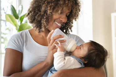 Happy mother bottle feeding her baby girl at home - SBOF03322