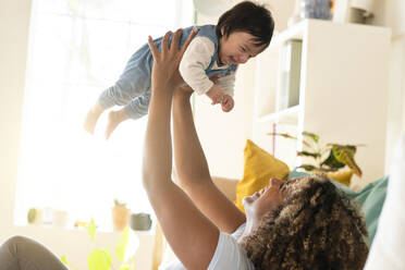 Happy mother picking up smiling baby at home in living room - SBOF03332