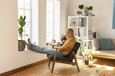 Father holding sleeping baby while sitting on armchair at home - SBOF03337