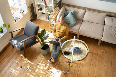 Father working on laptop while baby girl playing by him at home - SBOF03361